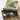 An open box of assorted dark chocolates displayed beneath its illustrated lid, which features a Christmas tree and wrapped gifts on a pale green background. The chocolates are arranged in dark brown molds, with some pieces wrapped in silver foil.